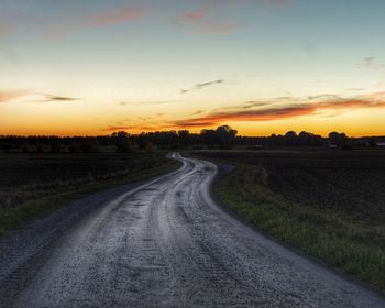 Road amidst field against sky during sunset