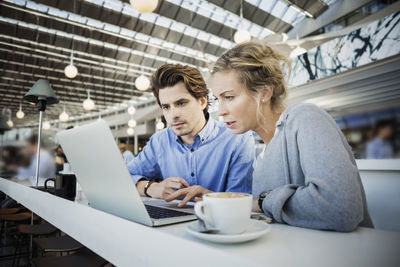 Business colleagues using laptop at airport cafe