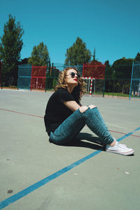 Young woman wearing sunglasses while sitting at playground during sunny day