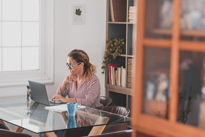 Full length of woman using phone while sitting on table