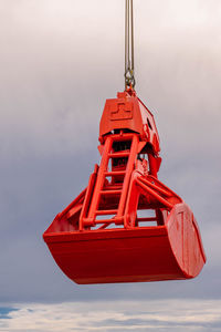 Close-up of red crane shovel hanging against sky