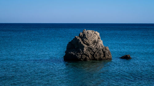 Rock formation in sea against clear blue sky