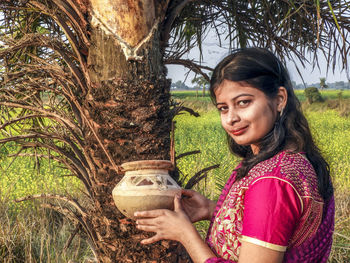 Portrait of a smiling young woman holding tree trunk