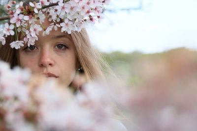 Close-up portrait of young woman standing by white flowers blooming outdoors