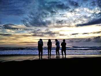 Silhouette people standing on beach against sky during sunset