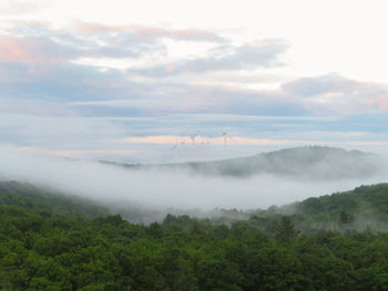 Scenic view of landscape and windmills against sky with pastel sunrise and morning fog