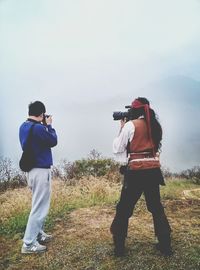 Rear view of man and woman photographing on field in foggy weather