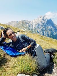 Portrait of smiling young woman sitting on mountain against sky