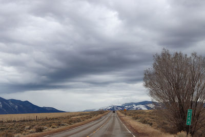 Road passing through landscape against cloudy sky