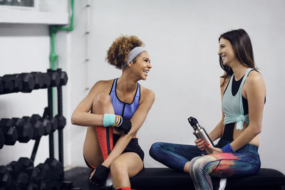 Happy female athletes talking while sitting on bench at gym