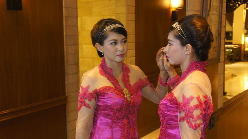 Young woman wearing tiara and pink dress reflecting on mirror