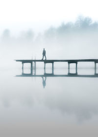 Silhouette man standing on lake against sky