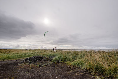 Couple standing on grassy field against cloudy sky