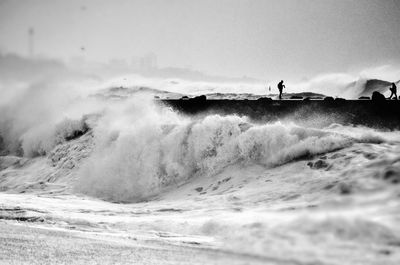 Sea waves splashing at shore against sky