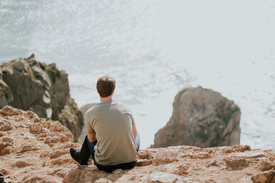 Rear view of man sitting on rock