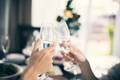 Cropped hands of female friends toasting champagne flutes at dining table