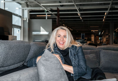 Confident woman with silver hair lounges on a grey sofa in a chic denim jacket