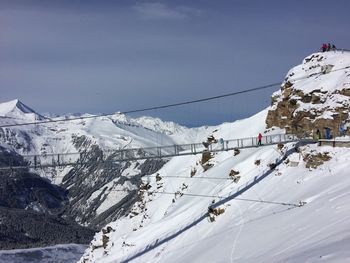 Footbridge by snow covered mountains against sky