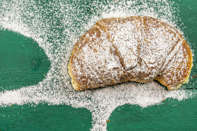 Freshly baked croissants with powdered sugar on a green rustic table ready for breakfast. top view