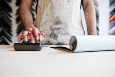 Male store owner using calculator while making financial bill in workshop