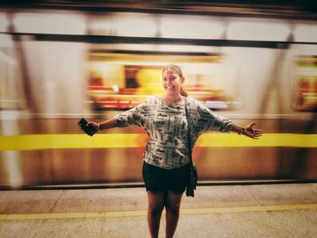 Portrait of smiling young man with arms outstretched standing at railroad station