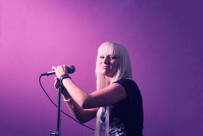 Young woman holding umbrella while standing against pink wall