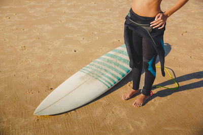 Low section of woman standing with surfboard at beach