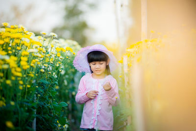 Cute girl standing by yellow flowering plants