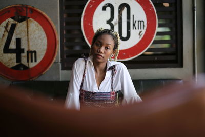 Portrait of young woman against speed limit sign