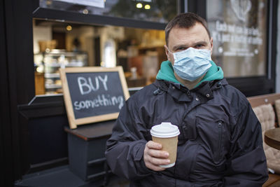 Portrait of man wearing mask holding coffee cup standing outdoors