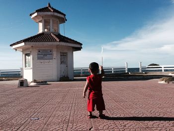 Rear view of boy standing on promenade by sea against sky