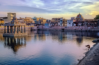 Buildings by river against sky in city