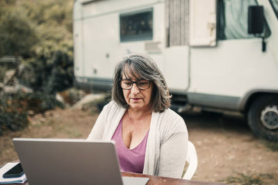Woman using laptop on table in front of motor home