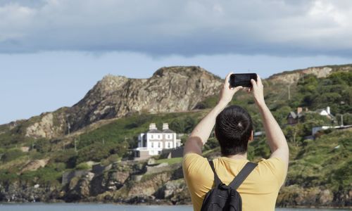 Rear view of woman photographing on mountain against sky