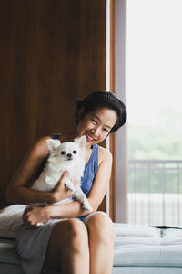 Portrait of cute girl sitting on sofa holding dog at home