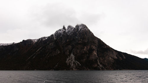 Scenic view of sea by mountain against sky