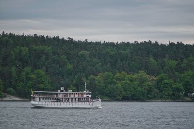 Boat sailing on river by trees against sky