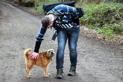 Man stroking dog while walking on dirt road