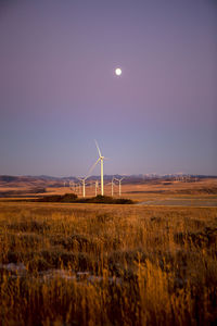 Wind turbines in field against dusk sky
