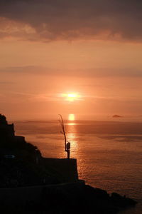 Silhouette man on sea against sky during sunset