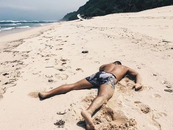 High angle view of shirtless young man lying at beach