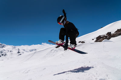 Low angle view of man skiing on snowcapped mountain against clear blue sky