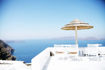 Chairs and table by sea against blue sky