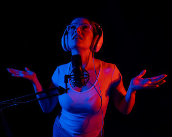 Portrait of young woman with arms raised standing against black background