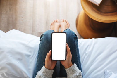 Low section of woman using mobile phone on bed at home