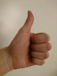 Cropped hand gesturing thumbs up sign against wall