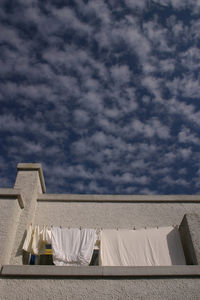 Low angle view of clothes drying at building balcony against cloudy sky