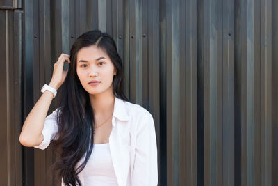 Portrait of confident young woman standing against wall