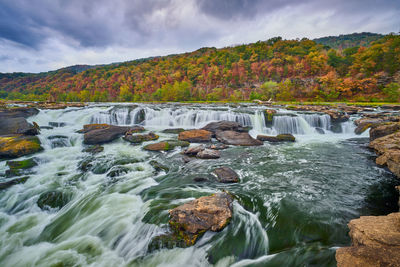 Water flowing through rocks in river against sky