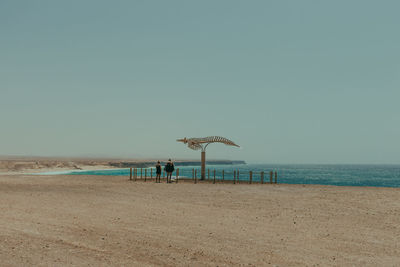 People standing at beach against clear sky